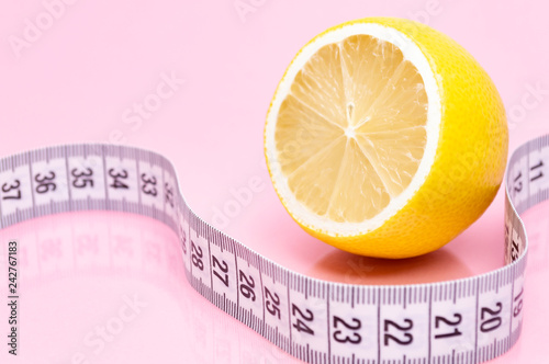 Sliced lemon and measuring tape on pink background. Diet concept.