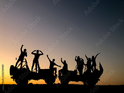 The silhouette of a group of people best friend having fun sitting and posing on a jeep over sunset background. friendship concept.
