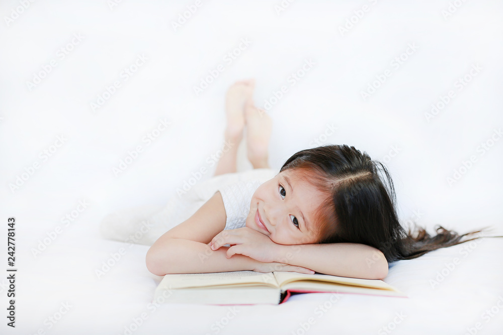 Adorable little Asian girl with hardcover book lying on bed and looking camera over white background. Adorable little Asian girl with hardcover book lying on bed and looking camera over white background.