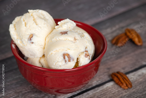 Delicious butter pecan ice cream served in a red bowl. Vintage wooden table background.