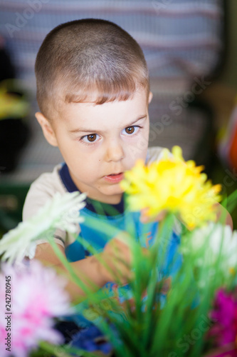 Top view cheerful little boy touching beautiful blooming flowers in vase at home.