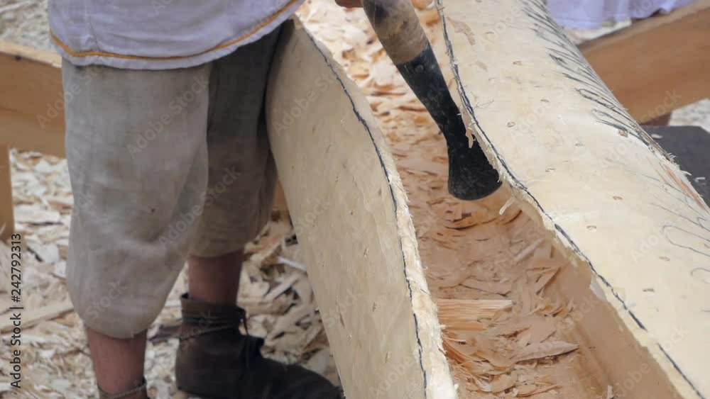 Ancient boatbuilder using adze to carve wooden sailboat. Reconstruction Ancient boatbuilder using adze to carve wooden sailboat. Reconstruction