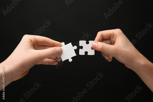 Female hands with pieces of puzzle on dark background