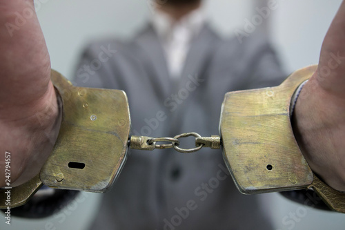 Close-up. Arrested man handcuffed hands at the back isolated on gray background. Prisoner or arrested terrorist, close-up of hands in handcuffs. photo