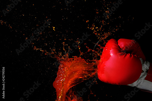 Hand in boxing glove with splashes of liquid on dark background