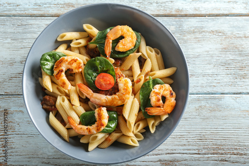 Tasty pasta with shrimps and tomatoes in bowl on wooden table