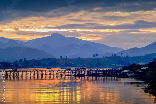 sunrise at Sangkhlaburi, river view morning on the river of old wooden bridge (Mon Bridge) with reflection on the water, mountain and colorful of yellow sun light in the sky,  Kanchanaburi, Thailand.