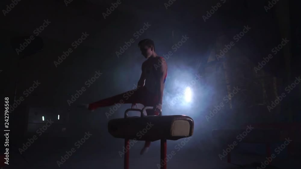 male gymnast athlete performs handstand and spin on Pommel horse on a dark background and smoke in slow motion. Olympic programme