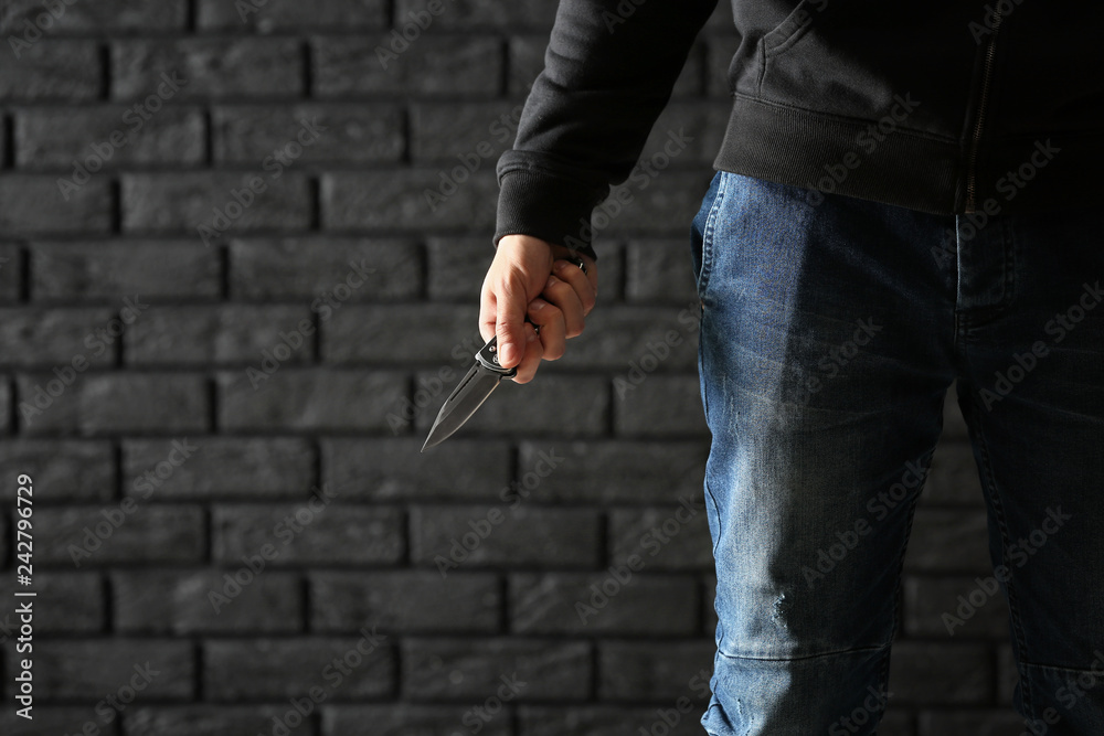 Naklejka premium Male criminal with a knife on dark brick background