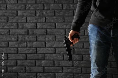 Male criminal with a gun on dark brick background