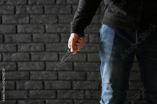 Male criminal with a knife on dark brick background