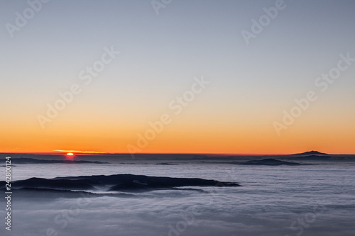 Beautiful sunset over a valley filled by fog with mountains and hills
