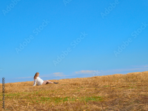 Beautiful pregnant woman in a white woolen sweater. Happy pregnant woman posing on a mown wheat field.