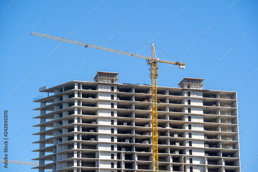 Construction of a high-rise building with a crane. The construction crane and the building against the blue sky.