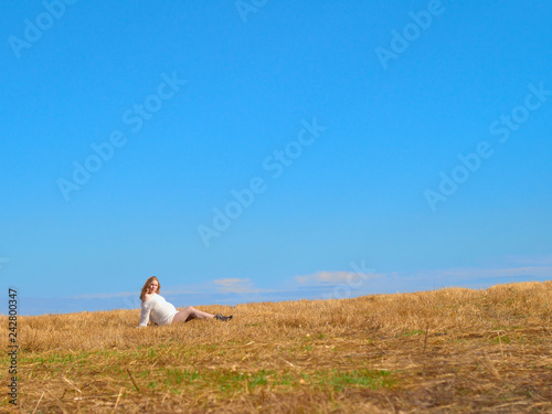 Beautiful pregnant woman in a white woolen sweater. Happy pregnant woman posing on a mown wheat field. © drouk