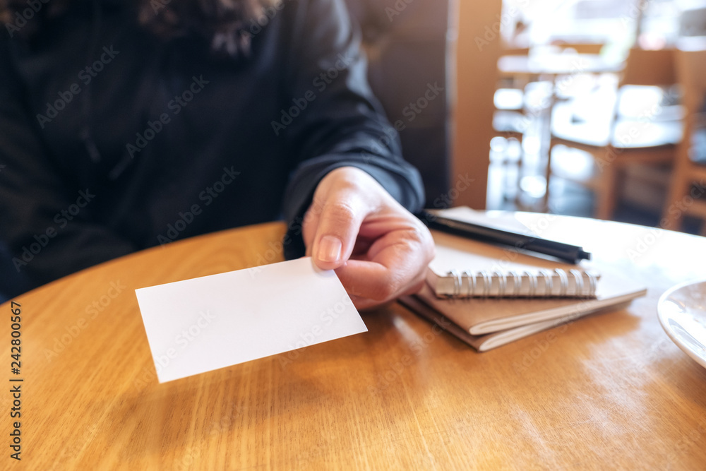A woman holding and giving a blank empty business card to someone with notebooks on wooden table A woman holding and giving a blank empty business card to someone with notebooks on wooden table