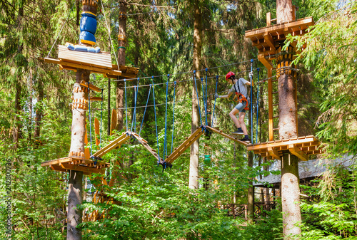 Teen boy on a ropes course in a treetop adventure park passing hanging rope obstacle