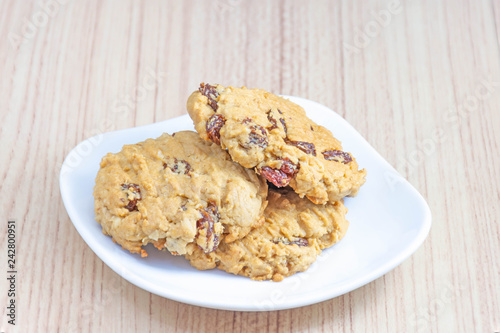Hearty raisin cookies put on a white plate. The background is tiled flooring mimics wood.