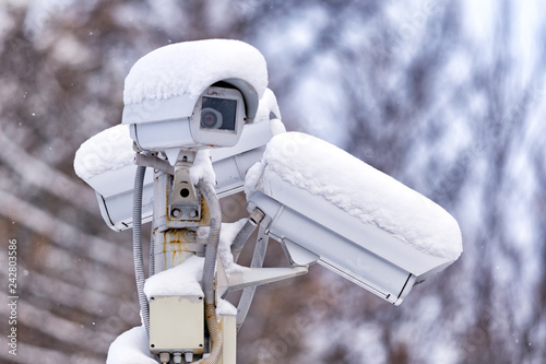 street outdoor surveillance CCTV camera on stand exterior closeup view with white snow cap cold season winter blurred background photo