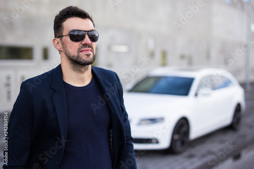 handsome business man in sunglasses posing with his car