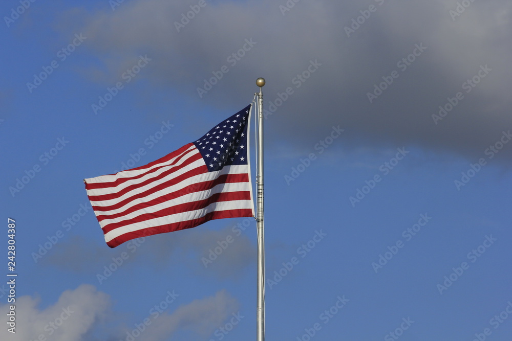 US Flag flying in the wind with blue sky and white clouds.