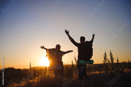 Silhouettes of two hikers with backpacks walking at sunset. Trekking and enjoying the sunset view