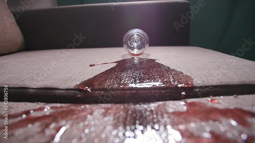 A glass of wine falls on the sofa and spills wine.