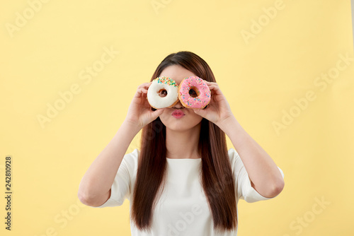 Attractive Asian woman holding two donuts with cute smiling expression over yellow background