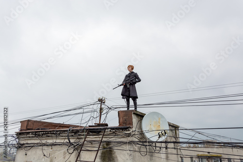 Young woman in modern black techwear style with rifle posing on the rooftop, portrait of redhead woman cyperpunk or post apocalyptic concept