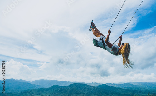 Blond girl swinging in the air over the mountains in summer photo
