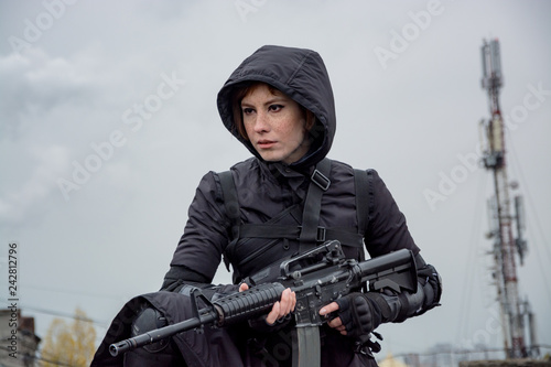 Young woman in modern black techwear style with rifle posing on the rooftop, portrait of redhead woman cyperpunk or   post apocalyptic concept