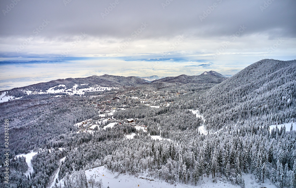 Aerial view over the spectacular ski slopes in the Carpathians mountains, Panoramic view over the ski slope Poiana Brasov ski resort in Transylvania,Romania,Europe,Pine forest covered in snow 