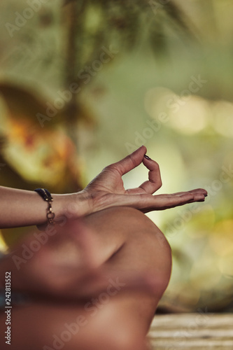 Young woman practicing yoga - meditation in the tropical garden. Focus on hand.