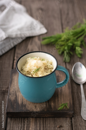 Porridge with butter, fresh herbs in a cup on a dark wooden board
