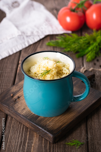 Couscous with butter, fresh herbs and tomatoes in a turquoise cup on a wooden table