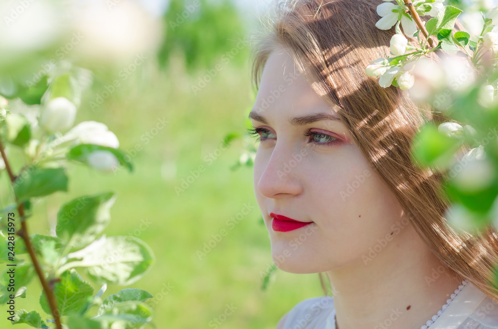 Portrait of a young beautiful woman in white top standing among blooming apple trees on a sunny day. Close-up with space for text. Portrait of a young beautiful woman in white top standing among blooming apple trees on a sunny day. Close-up with space for text.