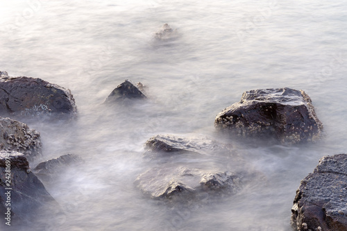 Misty, moody rocks in the water at sunset - long exposure.