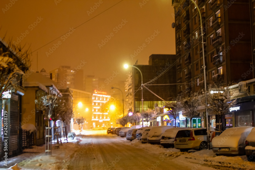 Strong snow fall on street of town in evening. Street covered with snow, and also trees and buildings. Center of Kragujevac town in Serbia.
