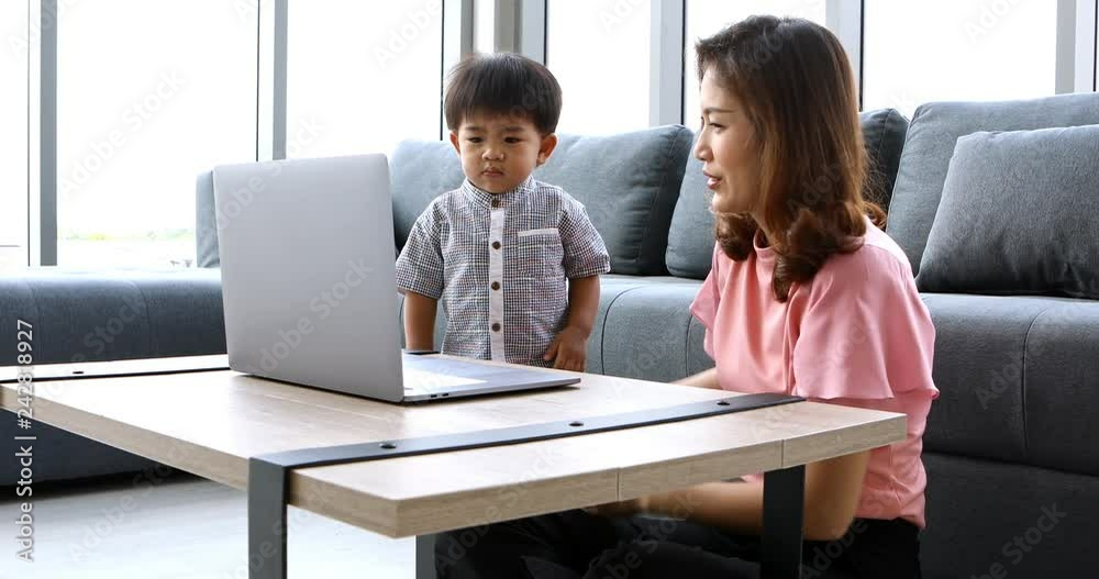 Asian mother and son sitting in living room, they using notebook to watch some video, then mom let son acting follow video, concept for mother and son using notebook. Asian mother and son sitting in living room, they using notebook to watch some video, then mom let son acting follow video, concept for mother and son using notebook.