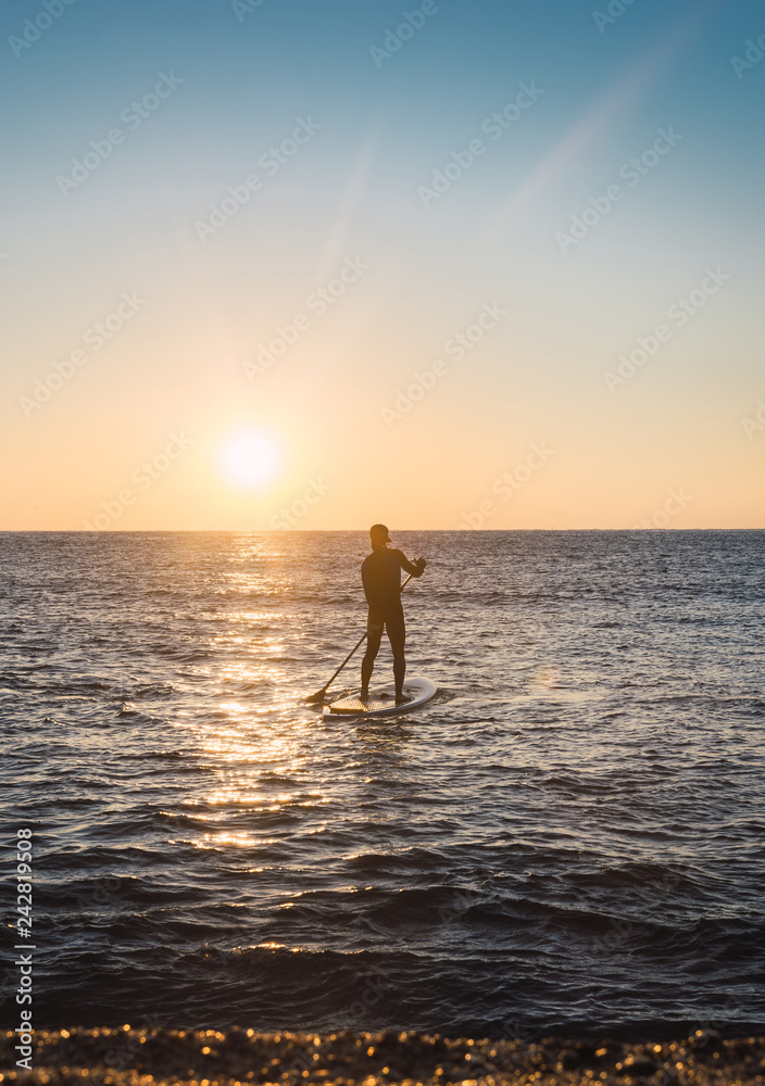 Man practicing paddle surfing with neoprene in a sunrise Man practicing paddle surfing with neoprene in a sunrise