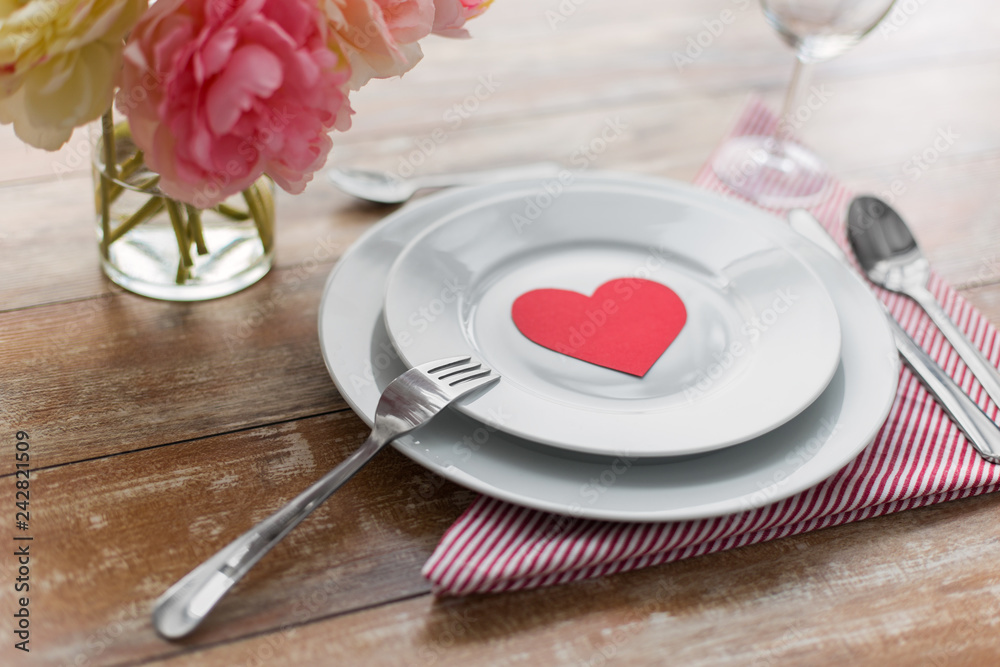 valentines day, table setting and romantic dinner concept - close up of plates with cutlery, flowers in vase and napkin valentines day, table setting and romantic dinner concept - close up of plates with cutlery, flowers in vase and napkin