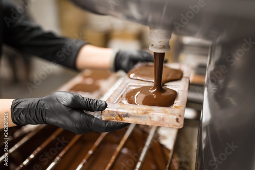 production, cooking and people concept - confectioner filling candy mold with chocolate at confectionery shop photo