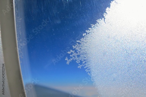 Beautiful ice crystals forming on an airplane window with clear blue sky in the morning. Soft focus. Transportation and background concept.