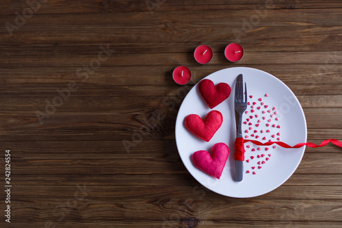  Valentines day table setting with plate, knife, candles, fork, red ribbon and hearts on the wooden background