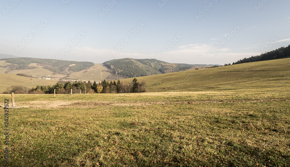 autumn landscape with meadows, hills, forest, smaller village and blue sky