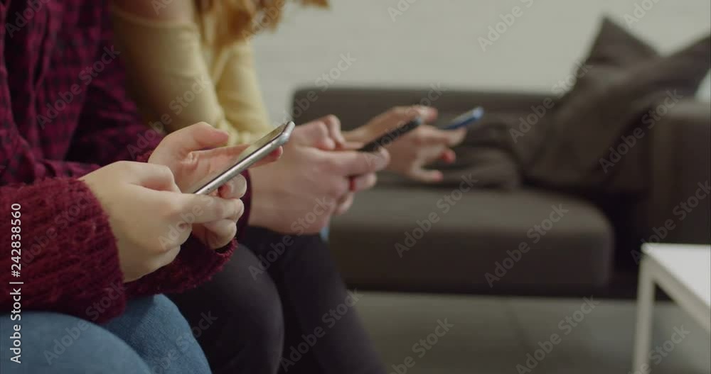 Close-up of diverse human hands holding smart phones, text masseging in online chat while sitting in row in domestic room. Midsection of cellphone addicted friends browsing social media content online Close-up of diverse human hands holding smart phones, text masseging in online chat while sitting in row in domestic room. Midsection of cellphone addicted friends browsing social media content online