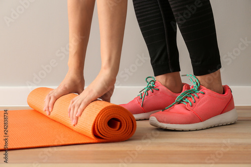 Young sporty woman with yoga mat in gym