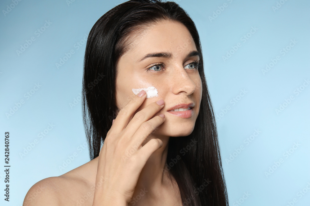 Portrait of beautiful young woman applying facial cream on color background Portrait of beautiful young woman applying facial cream on color background
