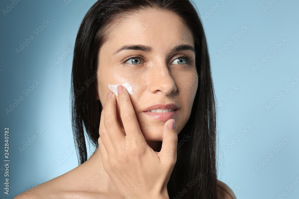 Portrait of beautiful young woman applying facial cream on color background Portrait of beautiful young woman applying facial cream on color background