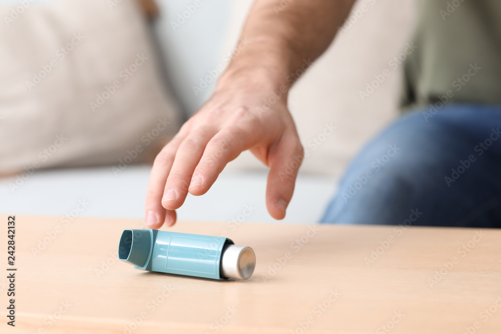 Young man with asthma attack taking inhaler from table, closeup Young man with asthma attack taking inhaler from table, closeup
